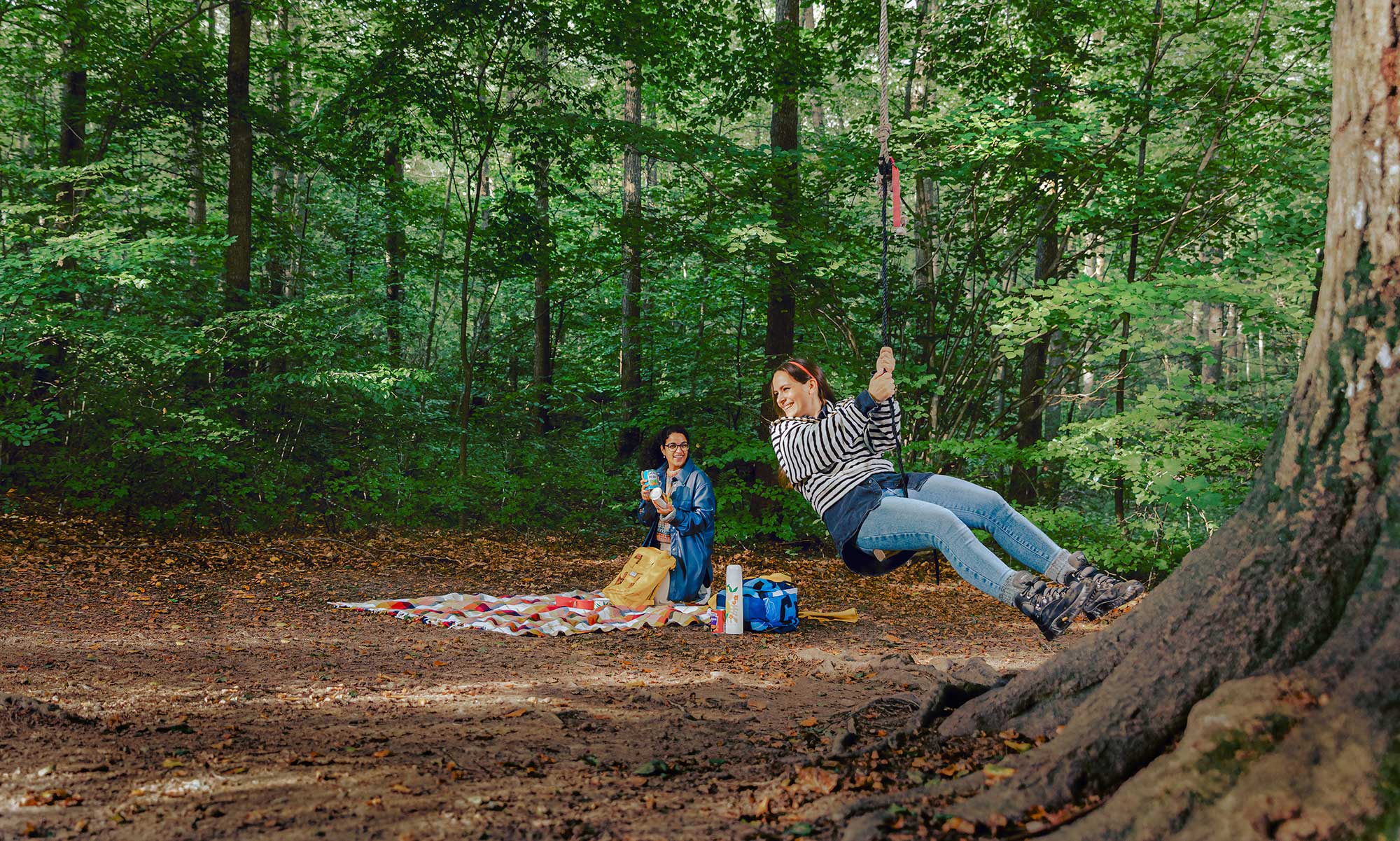 Two girls in the forest, one girl sitting at a swing.
