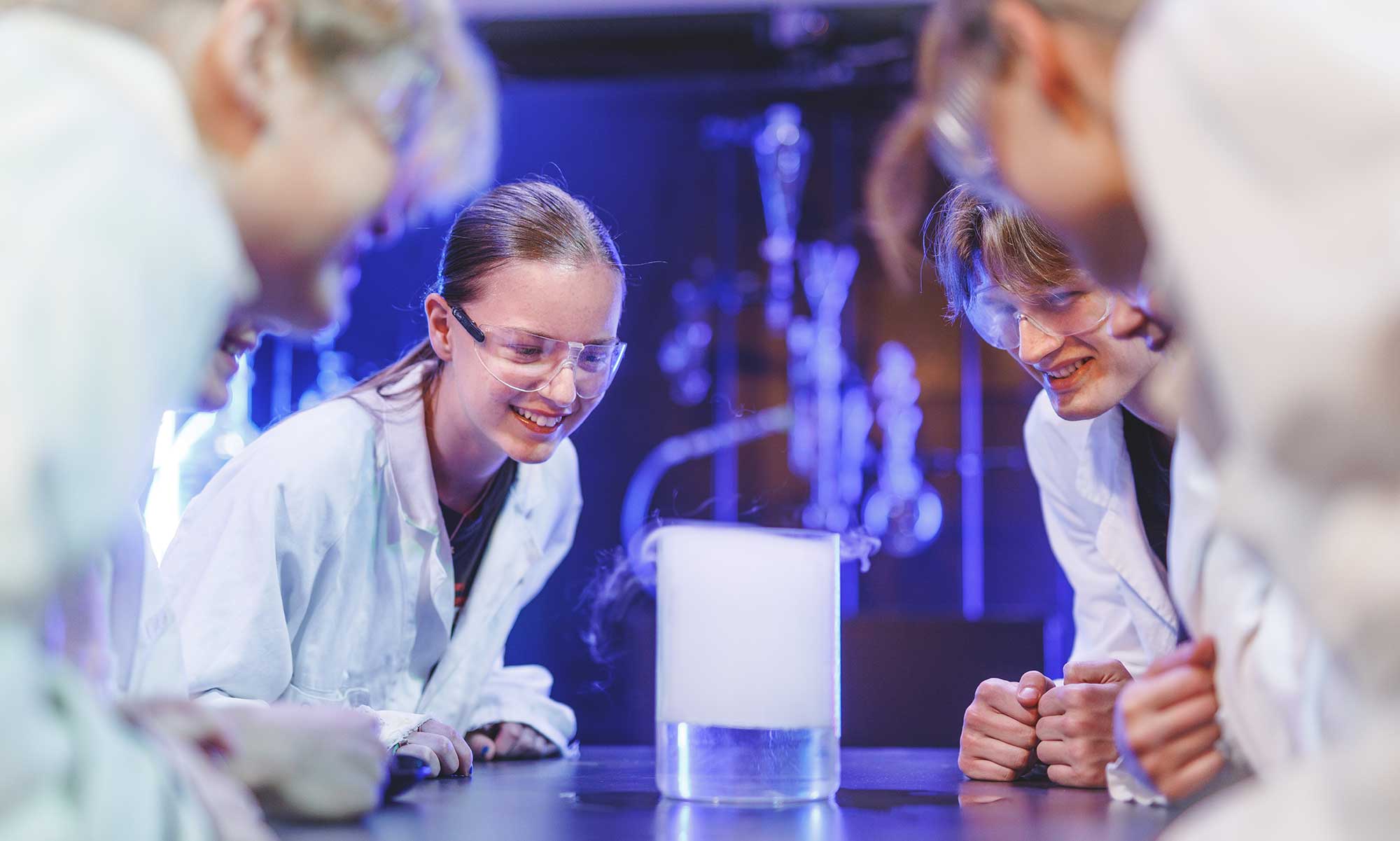 Students in a science environment  looking at smoke from a laboratory equipment.