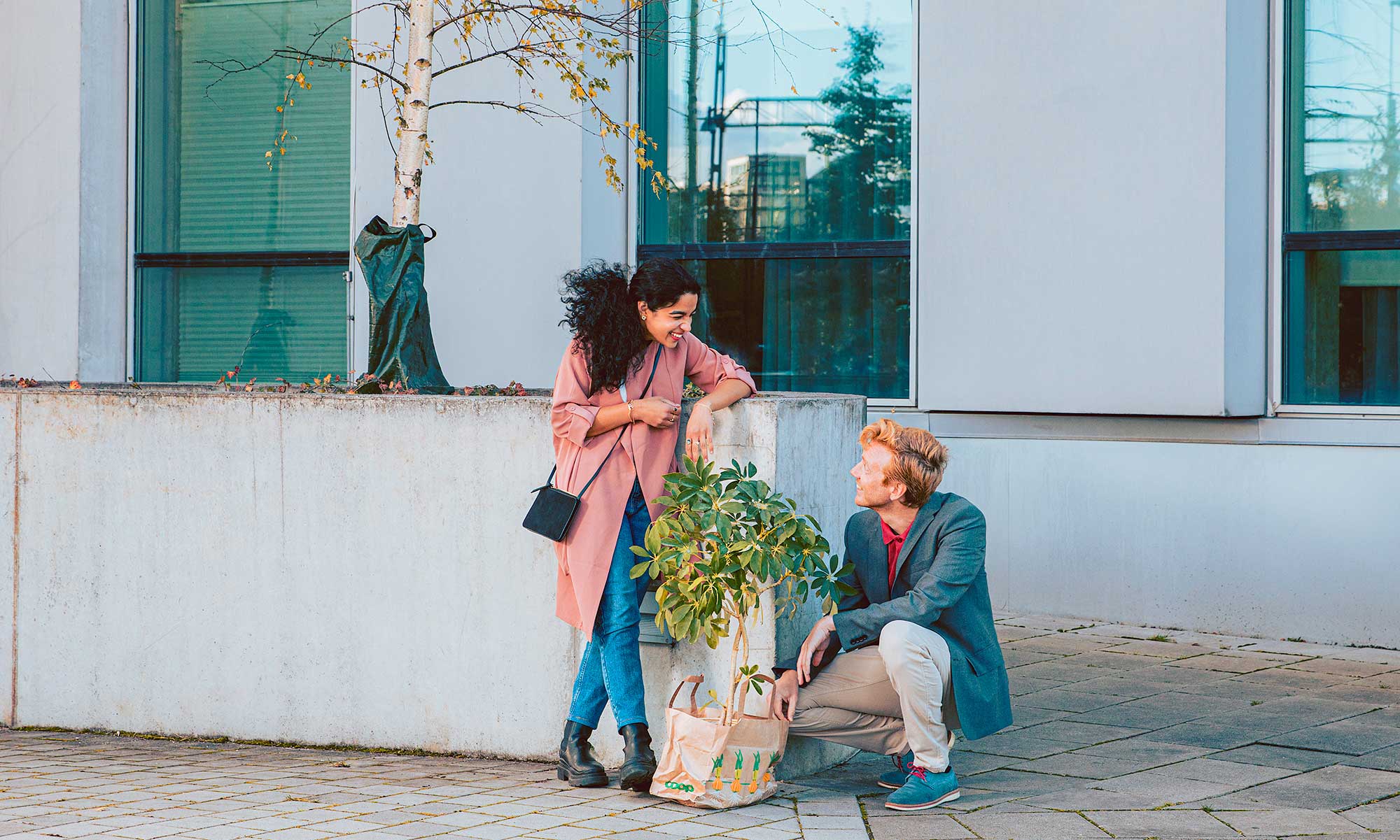 Man and woman standing in front of a building with a plant in a bag.